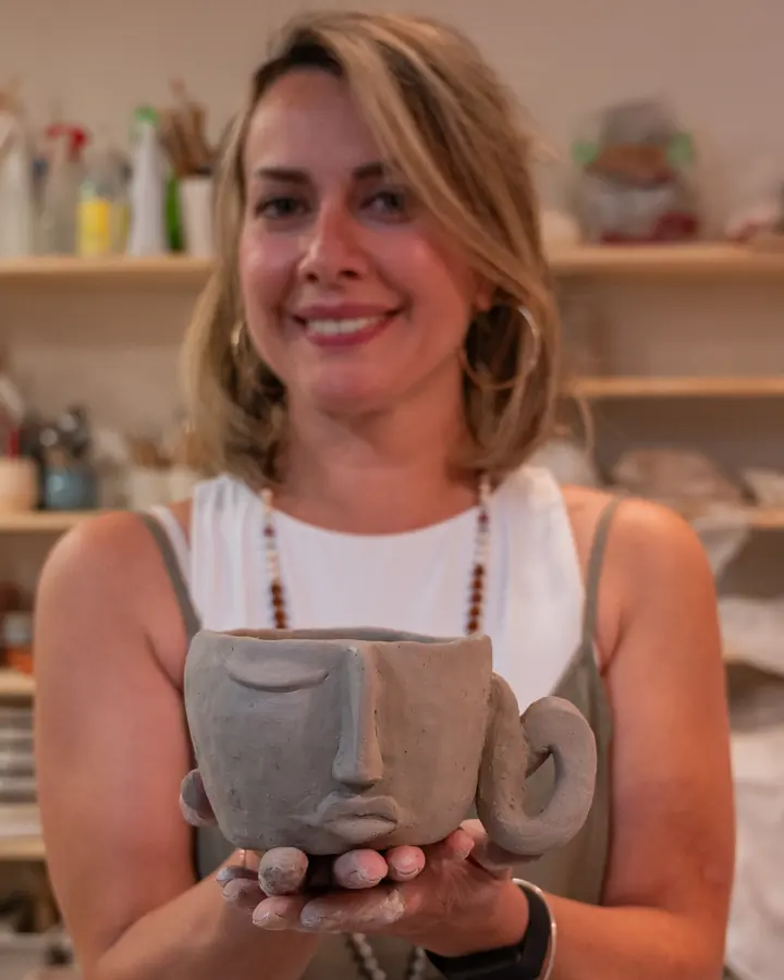 A student holding up the mug with a sculpted face that she made