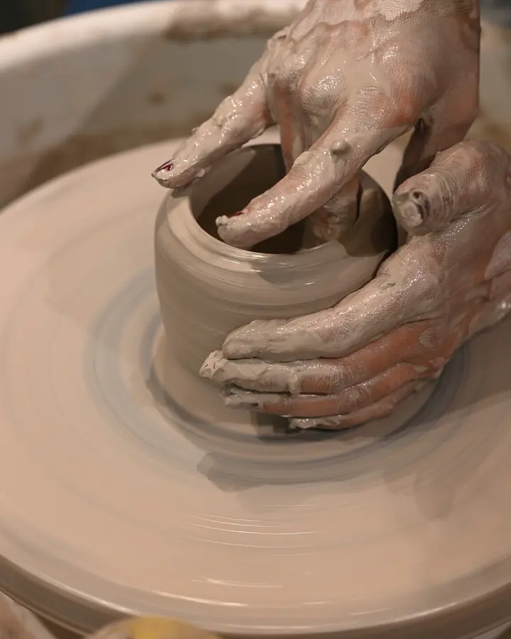 Clay-covered hands shaping a small pot on the wheel