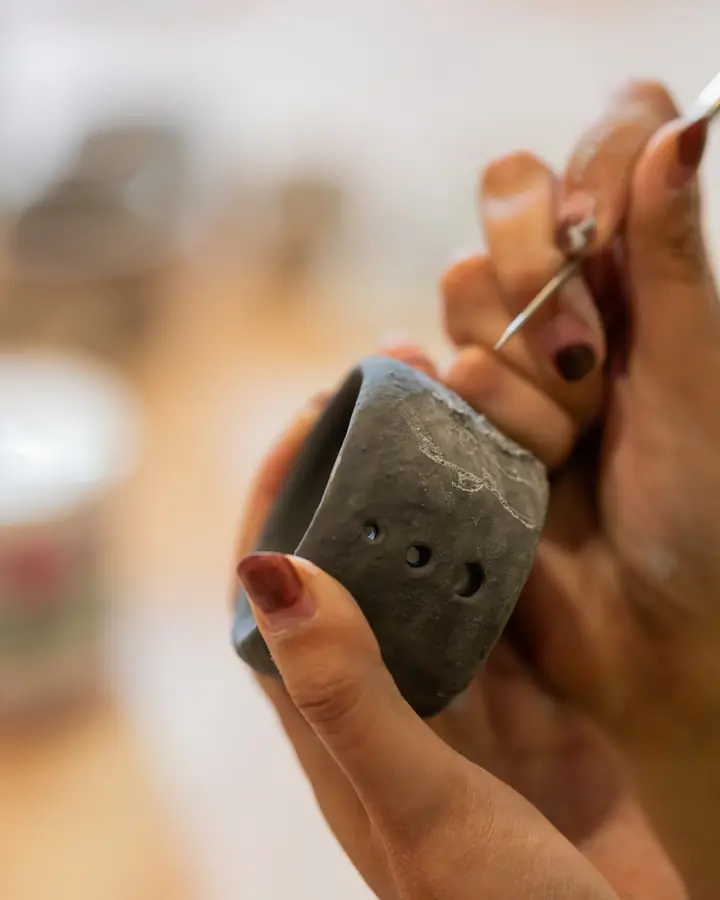 Hands carving holes into a small clay cup