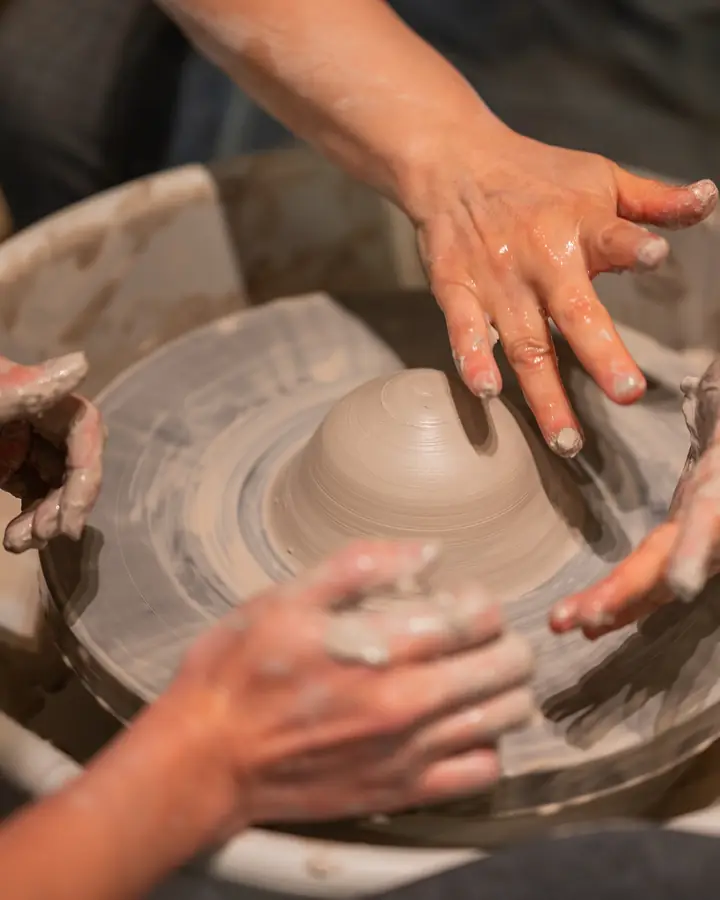 An instructor's hands and a student's hands shaping clay together
