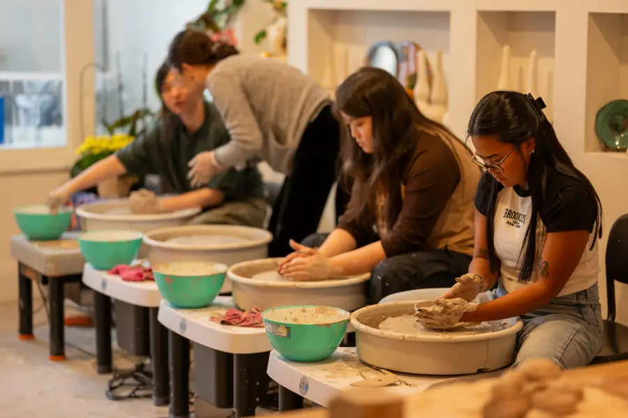Students shaping clay at a row of pottery wheels