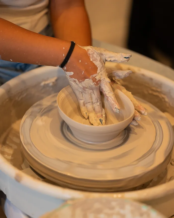 A beginner's hands opening a small bowl on the pottery wheel